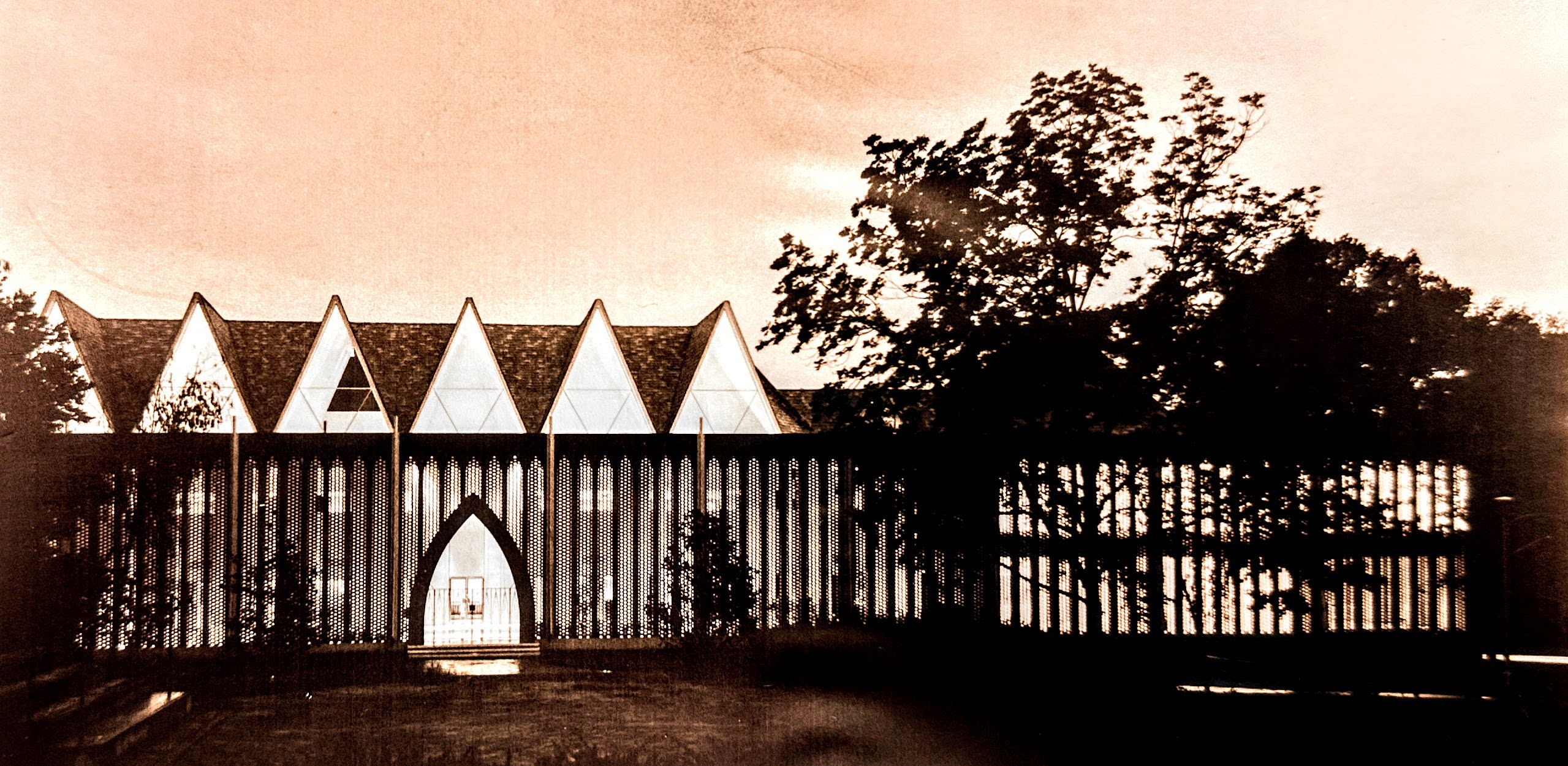 photograph of Dana Fine Arts Building from the front, includes three triangular windows on second level, brick exterior wall and pointed arch gateway. Taken in evening light